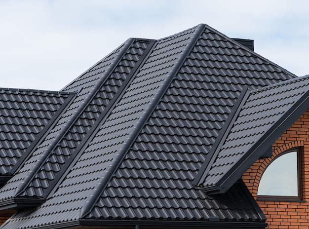 Das Haus, dessen Dach mit schwarzen Metallziegeln bedeckt ist Schwarzes Ziegeldach auf einem neuen Haus
