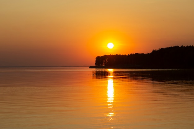 Das horizontale Foto des goldenen Sonnenuntergangs über dem Fluss oder dem Meer. Spiegelung im Wasser wie Feuer. Küste.