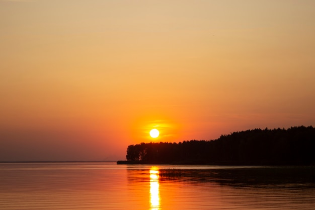 Das horizontale Foto des goldenen Sonnenuntergangs über dem Fluss oder dem Meer. Spiegelung im Wasser wie Feuer. Küste.