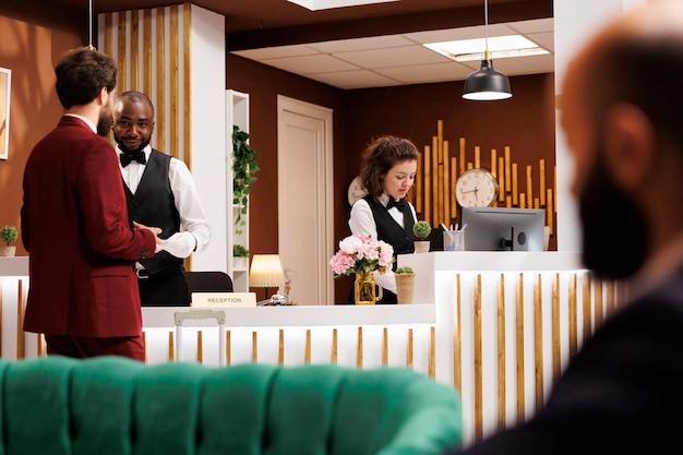 Das Hotelpersonal begrüßt den Geschäftsmann in der Lobby und sorgt für einen reibungslosen und effizienten Check-in. Rezeptionist teilt Luxusresort-Services mit, um Kunden bei wichtigen Geschäftsreisen zu helfen.