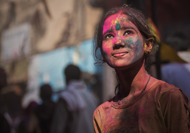 Das indische Mädchen, das mit Farben auf ihrem Gesicht geschmiert wird, wirft während der Holi Festivalfeier auf