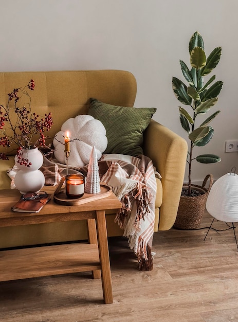 Foto das innere des wohnzimmers ist ein sofa mit einer decke eine bank mit dekor brennenden kerzen und ein bouquet von zweigen in einer vase gemütliches haus