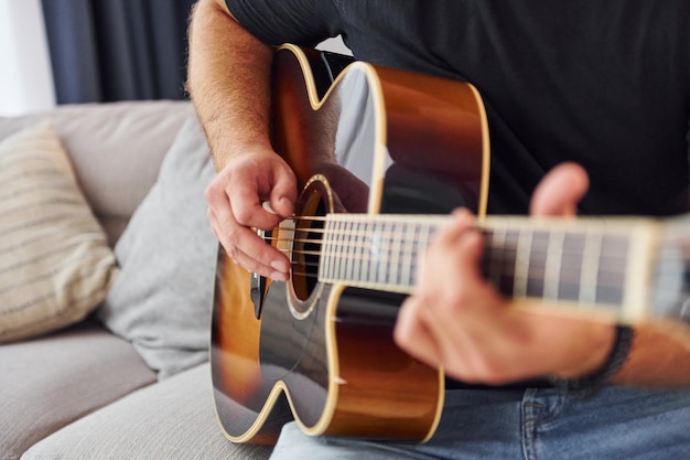 Das Instrument spielen Mann in Freizeitkleidung und mit akustischer Gitarre ist drinnen