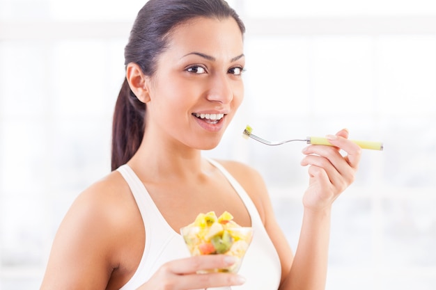 Das ist mein Lieblingsessen. Seitenansicht einer schönen jungen indischen Frau, die einen Obstsalat isst und lächelt