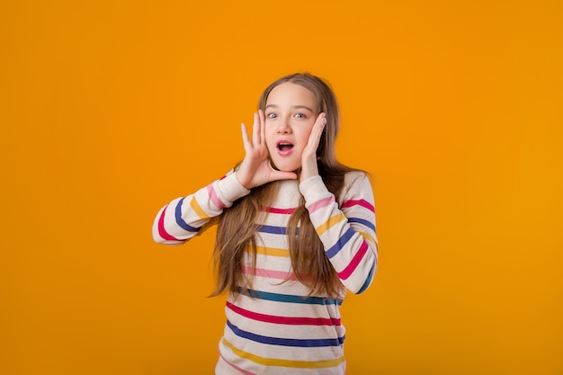 Das jugendlich Modell des jungen Mädchens wirft auf einem gelben Hintergrund in einer mehrfarbigen gestreiften Jacke auf. Emotionen, Raum für Text