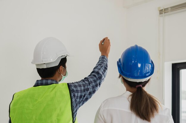 Das junge asiatische bauunternehmerteam des bauers trägt eine maske, während es die rekonstruierte konstruktion inspiziert, die renoviert oder auf defekt überprüft wird, bevor es an den kunden auf der baustelle übergeben wird arbeiterkonzeptxa