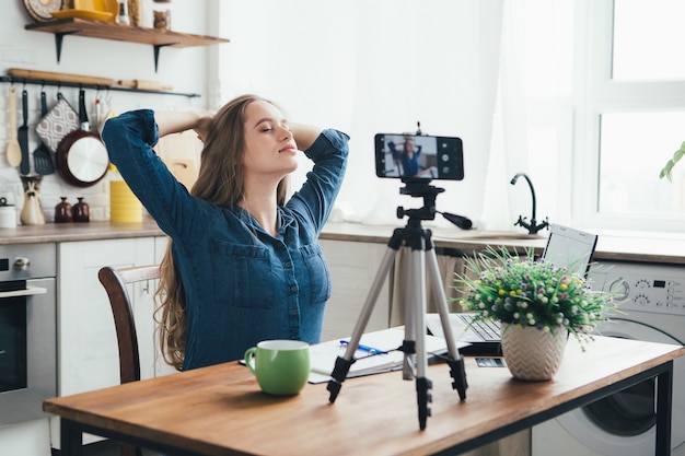 Das junge hübsche schwangere Mädchen arbeitet zu Hause im Selbstisolationsmodus in Quarantäne und zeichnet Videos auf ihrem Smartphone auf
