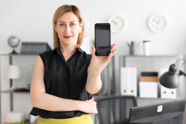 Das junge Mädchen, das im Büro steht und zeigt den Telefonschirm.