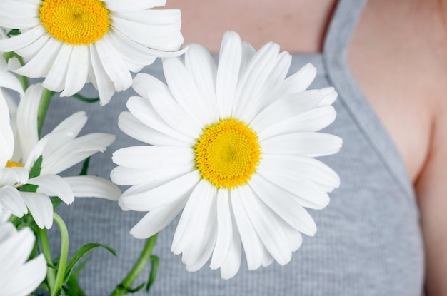 Das junge Mädchen in einem grauen Kleid hält einen Strauß weißer Gänseblümchen in ihren Händen Sommerblumen Kamille