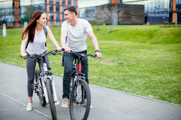 Das junge Paar, das ein Fahrrad anstrebt, fahren an einem sonnigen Tag in der Stadt