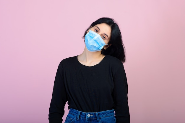 Das kaukasische Mädchen in der blau gefärbten schützenden Gesichtsmaske. Porträt schoss über rosa Hintergrund. Konzept zum Schutz vor Viren und Umweltverschmutzung.