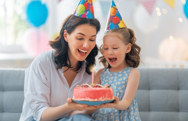Das Kind bläst die Kerzen auf dem Kuchen aus. Mutter und Tochter feiern Geburtstag.