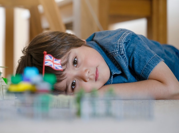 Das Kind, das auf den Teppich sich entspannt und spielt mit Soldaten und Figürchenspielzeug legt, erntete das Schusskind, das seine Plastikspielwaren betrachtet