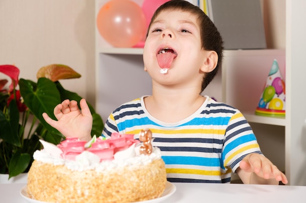 Das Kind feiert einen Geburtstag, lacht und leckt einen Geburtstagskuchen