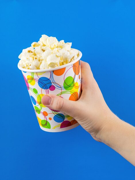 Das Kind hält ein buntes Glas Popcorn auf einer blauen Oberfläche.