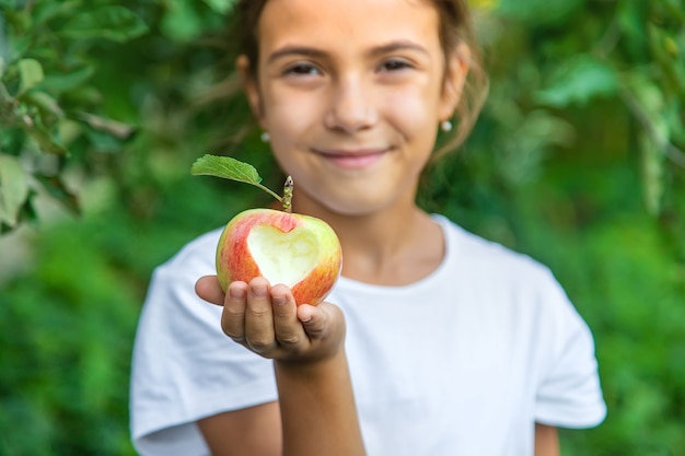 Das Kind isst einen Apfel im Garten. Selektiver Fokus. Kind.