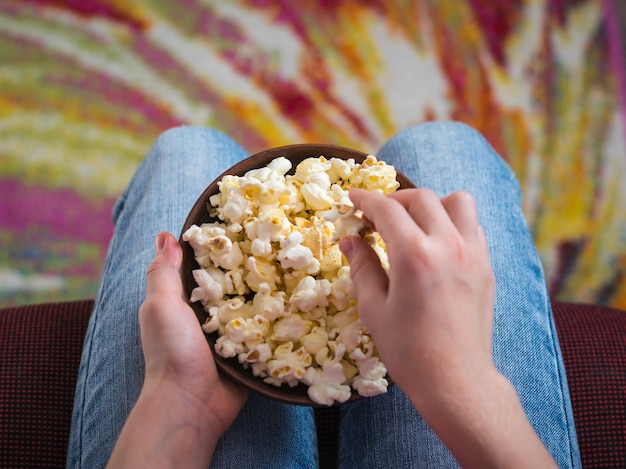 Das Kind isst Popcorn aus einer Tonschale und sitzt auf einem roten Stuhl