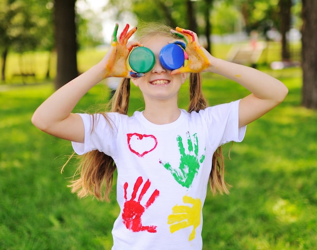 Das Kind ist mit bunten Fingerfarben Kleidung im Park lächelnd beschmiert.