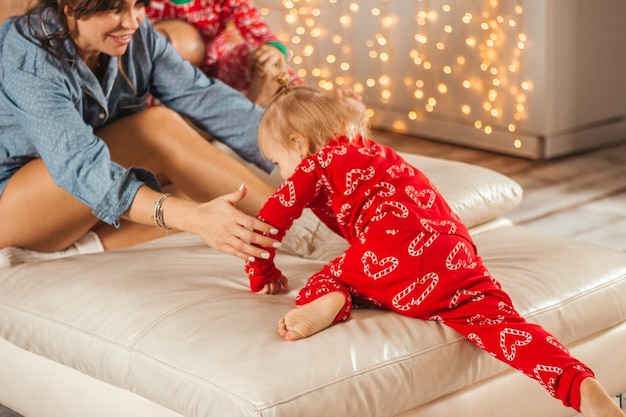 Das Kind klettert zu Weihnachten im Pyjama auf die Couch zu seiner Mutter