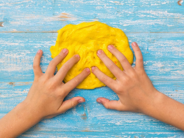 Das Kind knetet mit den Fingern einen Kreis aus gelbem Schleim auf einem blauen Tisch
