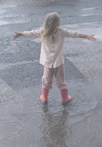 das kind läuft nach einem regen auf pfützen in gummistiefeln