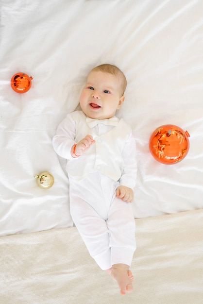 Das Kind liegt auf dem Bett im Schlafzimmer, umgeben von Spielzeugbällen für Weihnachtsbäume und lacht