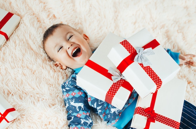 Das Kind liegt auf der flauschigen flauschigen Decke, neben ihm ein Haufen Geschenke, das Kind freut sich sehr