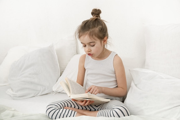 Das Kind liest ein Buch im Schlafanzug auf einem Bett. Kinderentwicklungs- und Lernkonzept.