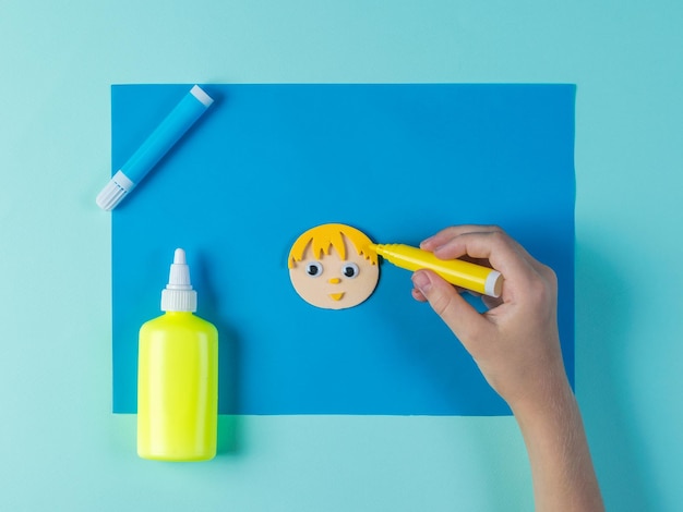 Das Kind malt die Haare auf Papierapplikationen in Form eines Mannes