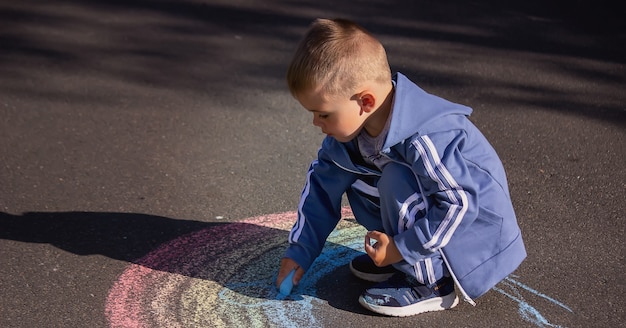 Das Kind malt mit Kreide die Farben des Regenbogens auf den Asphalt