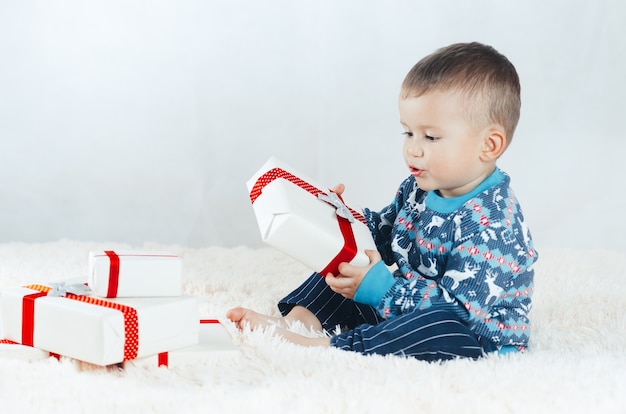 Das Kind sitzt auf dem Bett und spielt mit Geschenken verpackt, Silvester im Rentierpullover