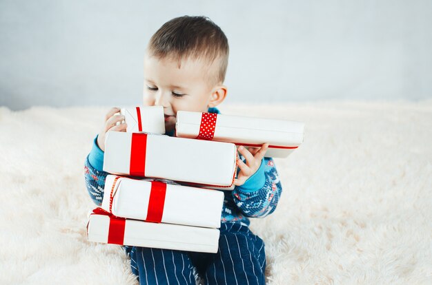 Das Kind sitzt auf dem Bett und spielt mit Geschenken verpackt, Silvester im Rentierpullover