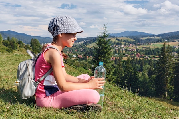 Das Kind sitzt auf einem Hügel vor dem Hintergrund der Berglandschaft