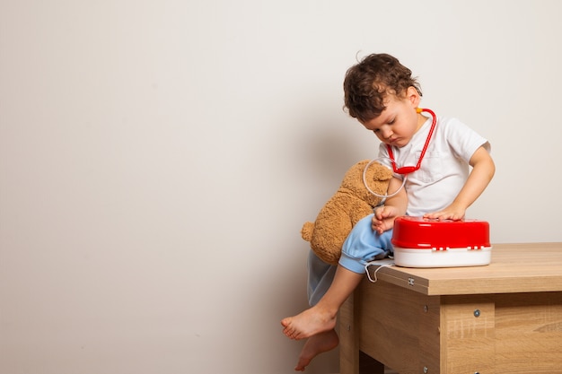 Das Kind spielt im Arzt mit einem Teddybär und einem Spielzeug-Erste-Hilfe-Kasten