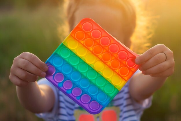 Das Kind spielt mit einem bunten Regenbogenspiel Mohn. Silikon zappeln Nahaufnahme.
