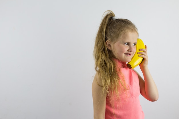 Das Kind spricht scherzhaft am Bananentelefon und lacht. Spiele und Aktivitäten für Kinder