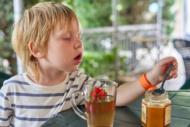 Das Kind trinkt Tee mit Honig auf der Sommerveranda