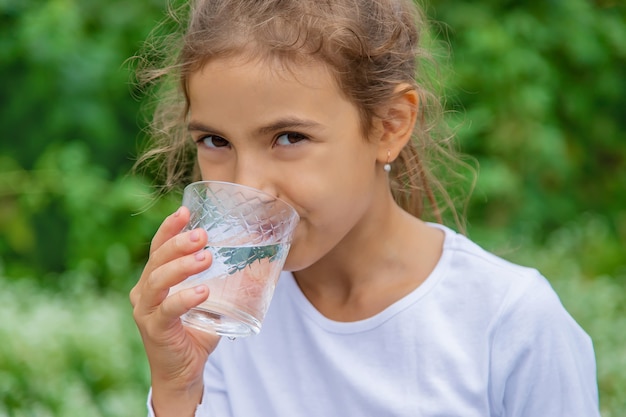 Das Kind trinkt Wasser aus einem Glas. Selektiver Fokus.