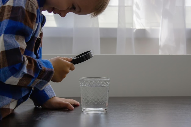 Das Kind untersucht das Wasser mit einer Lupe in einem Glas Kid