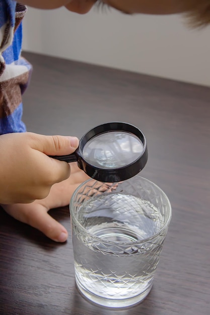 Das Kind untersucht das Wasser mit einer Lupe in einem Glas Kid