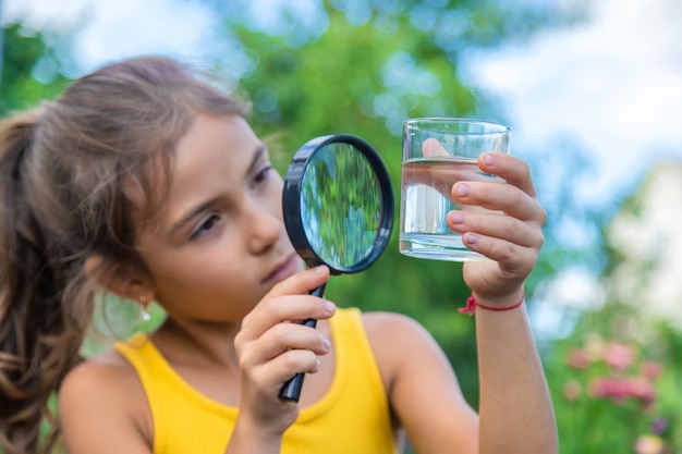 Das Kind untersucht ein Glas Wasser mit einer Lupe. Selektiver Fokus.