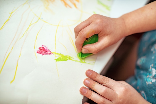 Das Kind zeichnet eine Blume auf Papier mit Wachsmalstiften, die mit seinen eigenen Händen hergestellt wurden