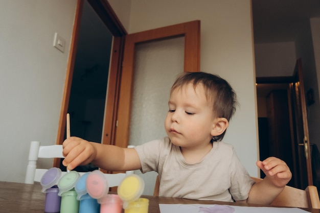 das kind zeichnet mit pinsel und bunter gouache am tisch sitzend zu seiner mutter