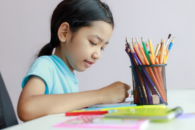 Das kleine asiatische Mädchen, das Hausarbeit tuend setzt, benutzen Farbbleistift, um auf Papier zu zeichnen