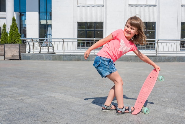 Das kleine glückliche Mädchen, das lernt, auf ein Skateboard zu gehen Ein Konzept für einen aktiven Lebensstil