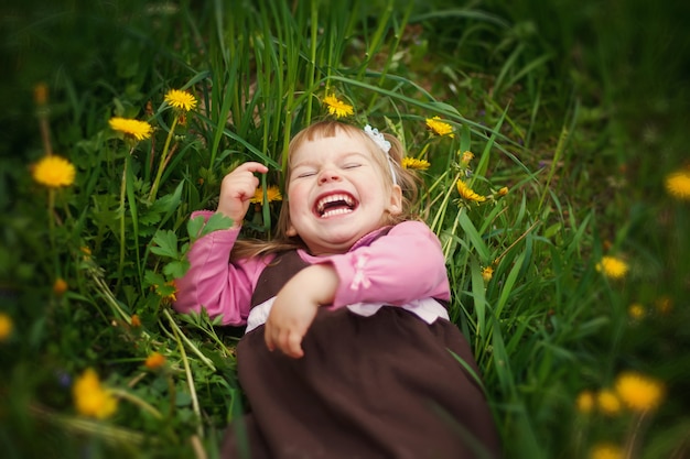 Das kleine glückliche Mädchen liegt im Gras und lacht