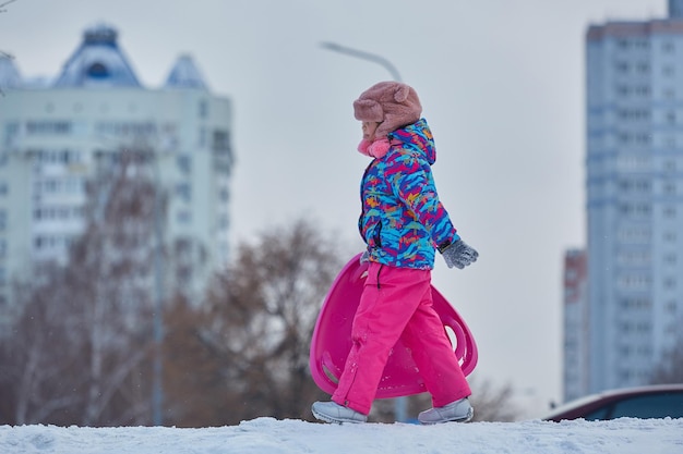 Das kleine Mädchen, das auf Schnee reitet, schiebt in der Winterzeit