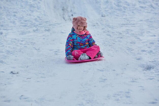 Das kleine Mädchen, das auf Schnee reitet, schiebt in der Winterzeit