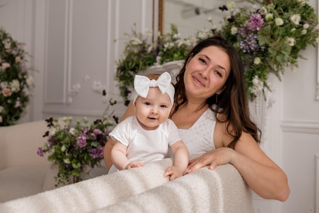 Das kleine Mädchen steht mit ihrer brünetten Mutter auf der Couch und schaut in die Kamera Fröhliche Kindheit