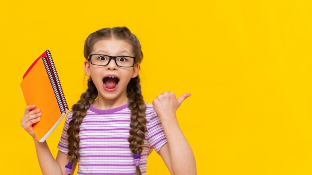 Das kleine Mädchen zeigt mit dem Finger zur Seite und lächelt Ein Schulmädchen mit Zöpfen und Brille auf isoliertem Hintergrund